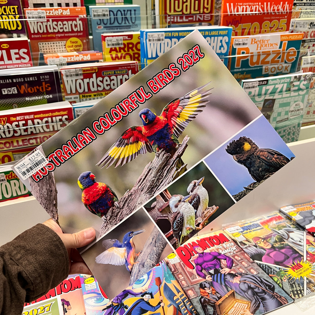 A hand holds a Cal titled 'Australian Colourful Birds 2027' featuring colorful bird illustrations on the cover