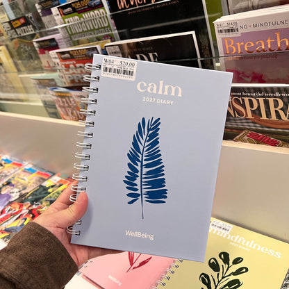 A hand holds a light blue spiral-bound 2027 diary titled 'calm' with a blue fern leaf illustration on the cover