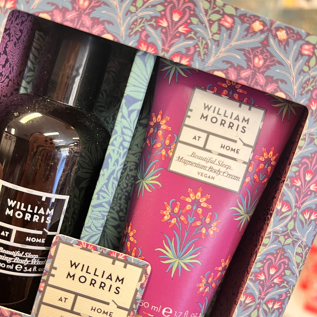 William Morris At Home gift set featuring a 'Beautiful Sleep Magnesium Body Cream' in a pink floral tube, a dark amber body wash bottle, and a decorative patterned box.