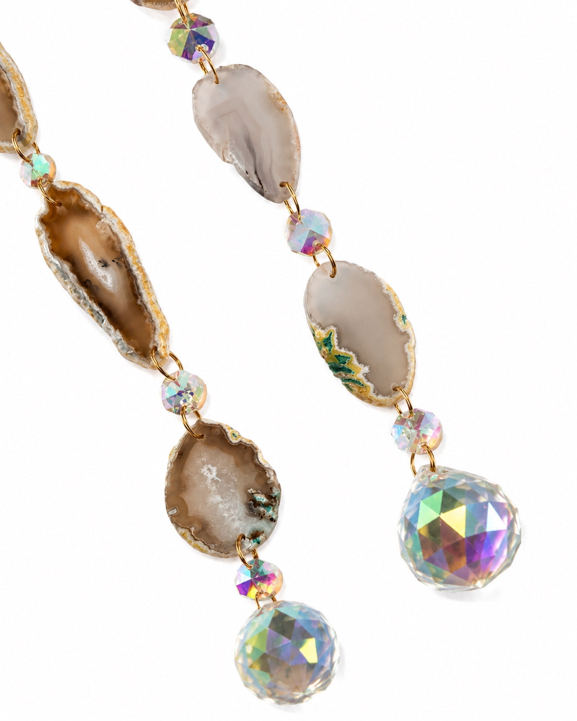 Close-up of neutral natural agate slice pendants and faceted rainbow crystal prism balls hanging from a golden crescent moon dream catcher.