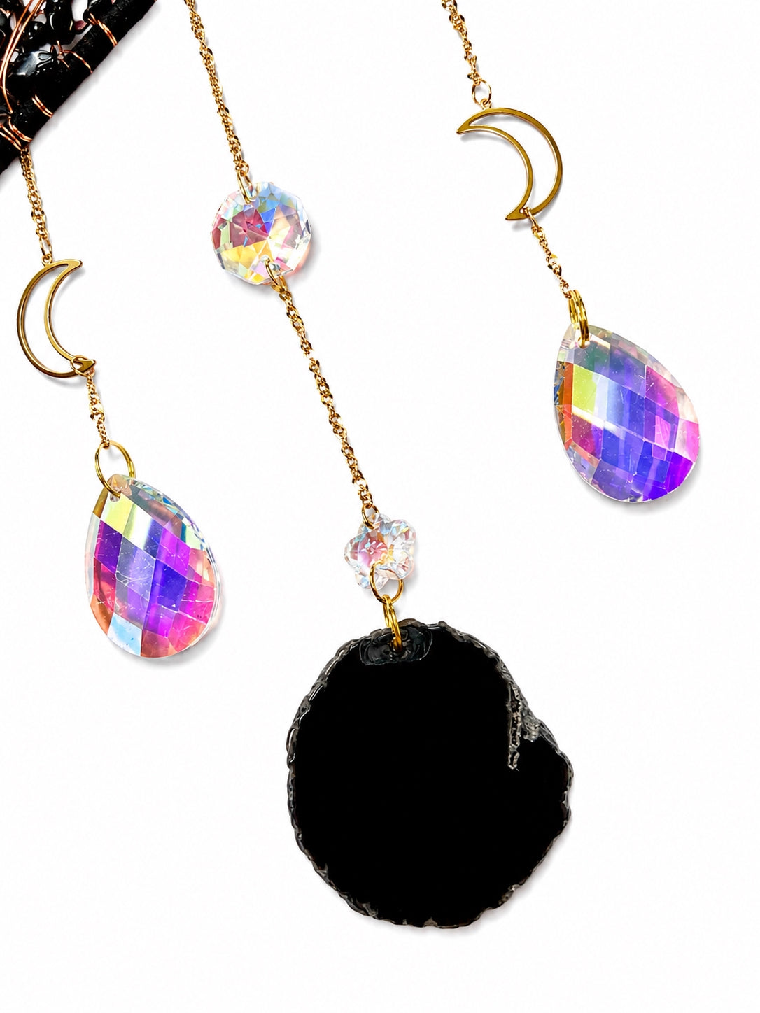 Close-up of a black natural agate slice, iridescent crystal prism and delicate bead chains from a star-shaped crystal suncatcher.