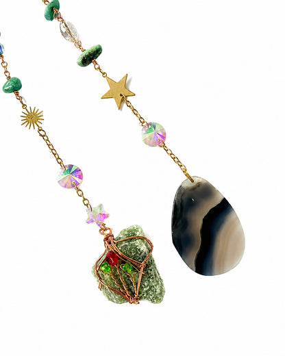 Close-up of colourful gemstone bead strands and dark natural stone pendants hanging from a turquoise crescent moon crystal dream catcher.