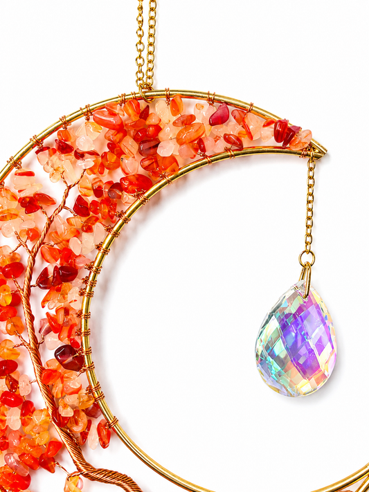 A crescent moon-shaped gold wire dream catcher decorated with orange and red stone chips, featuring a dangling iridescent teardrop crystal on a white background.