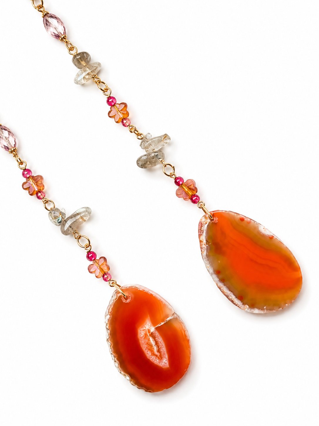 A beaded hanging pendant featuring two large teardrop-shaped orange agate pendants, separated by gold chains with small pink, orange, and clear crystal beads, shown on a white background.