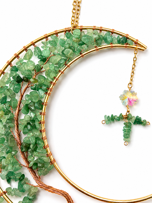Gold crescent moon dream catcher with green faceted gemstone accents and a dangling floral charm, shown on a white background.