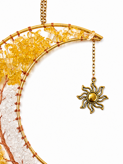 A close-up of a gold-toned crescent moon dreamcatcher with yellow and white beads, wrapped in copper wire, and a dangling sun charm on a white background.