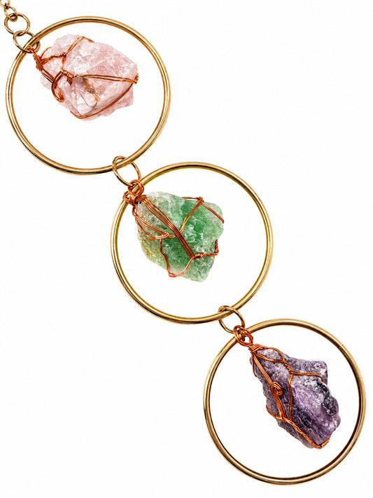 Close-up of colourful natural crystal stones wrapped with copper wire and displayed inside gold-toned circular frames.