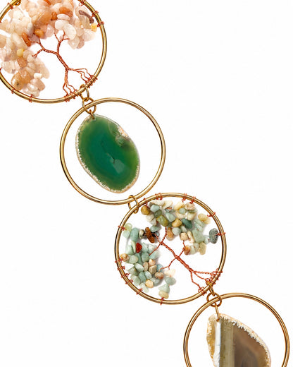 Close-up of a natural crystal window hanging with a green stone, multicoloured tree of life and gold-toned wire frames.