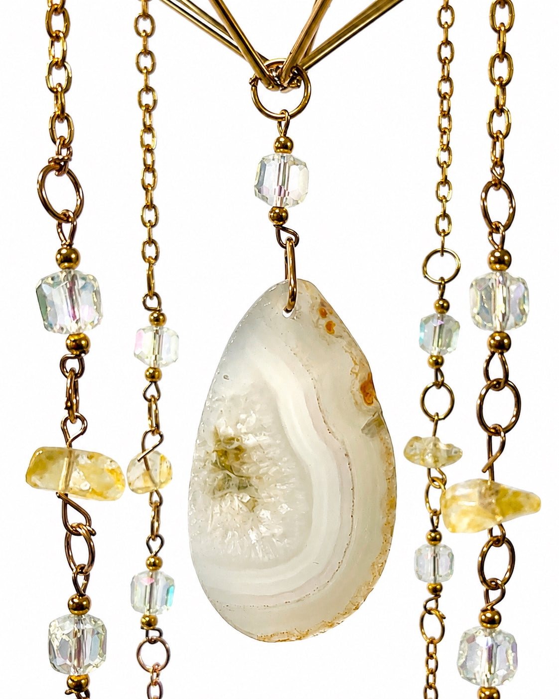 Close-up of a pale natural agate slice surrounded by delicate gold-toned chains, gemstone beads and hanging crystal prisms.
