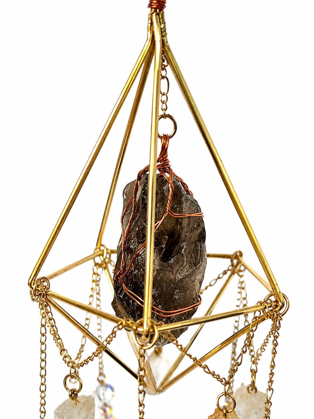 Close-up of a dark natural crystal suspended inside a gold-toned geometric frame with delicate wire and chain details.