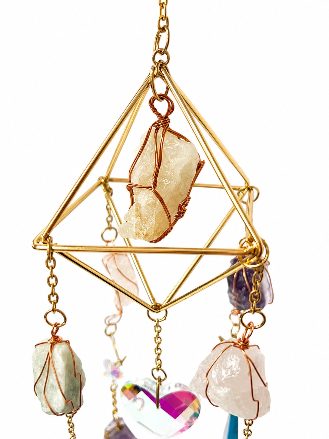 Close-up of a gold-toned geometric suncatcher frame featuring a wire-wrapped natural crystal and delicate hanging chains.