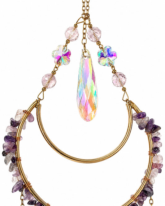 Close-up of a teardrop-shaped crystal suncatcher decorated with colourful gemstone chips, iridescent beads and gold-toned wire.