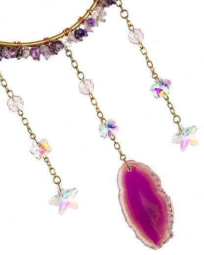 Close-up of iridescent crystal chains and a vibrant pink agate slice pendant on a handcrafted natural crystal suncatcher.