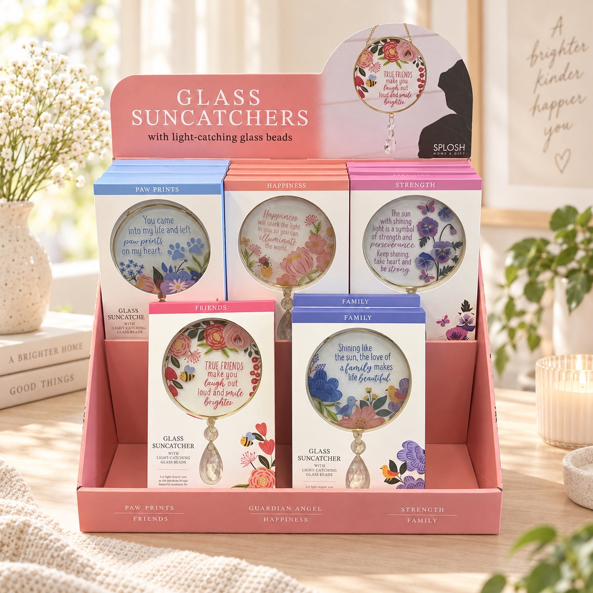 A pink retail display box holding several boxed glass suncatchers with floral artwork and text such as Paw Prints,  and Strength. 
