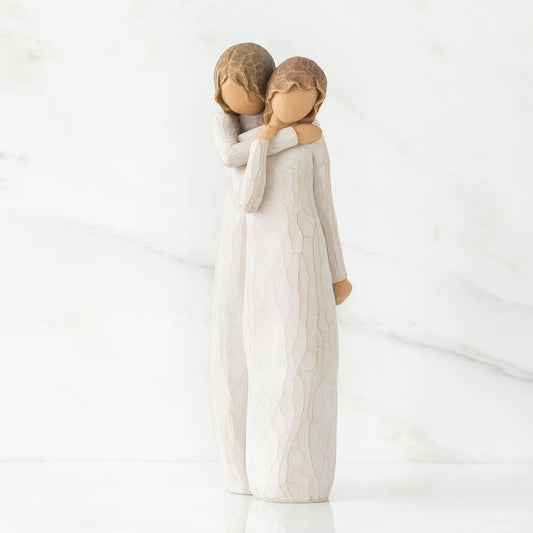 A Willow Tree figurine of a mother and daughter embracing, standing on a white reflective surface against a white marble background.